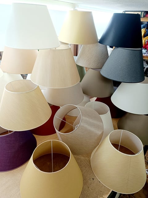 Collection of lamp shades in various colors and sizes displayed on a table, including cream, white, navy, and purple options