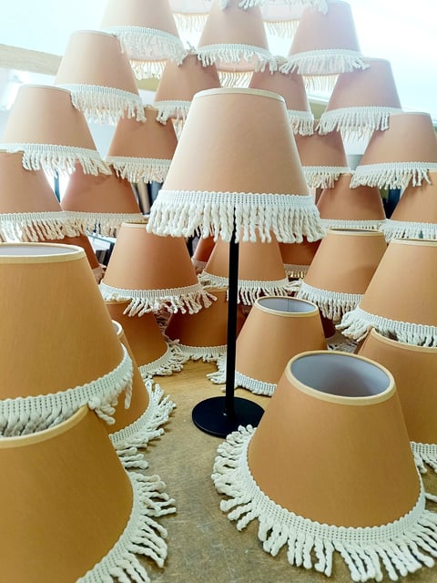 Collection of beige lampshades with white fringe trim arranged densely around a black floor lamp with white shade