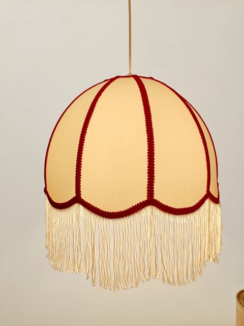 Vintage-style hanging pendant light with cream fabric shade, burgundy scalloped trim, and cream fringe tassel hanging from gold cord