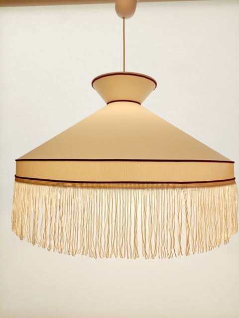 Vintage-style pendant light with cream fabric shade and beaded fringe trim hanging from ceiling