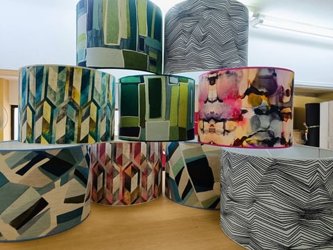 Collection of cylindrical fabric storage containers with various geometric and abstract patterns arranged on a wooden surface.
