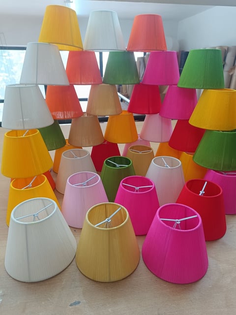 Collection of colorful fabric lampshades in various bright colors including pink, yellow, green, orange, and red arranged on display